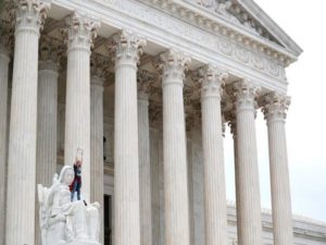 Protester stands on lap of "Lady Justice" with "Believe Survivors" sign as demonstrators storm steps and doors of the U.S. Supreme Court as Judge Kavanaugh is being sworn in as justice inside in Washington