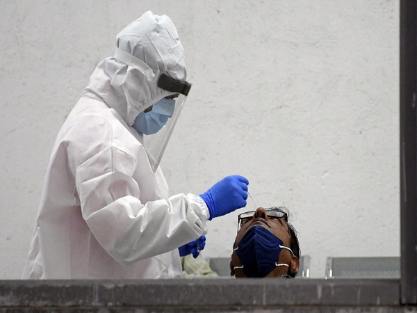 A health worker wearing a PPE kit collects swab sample of a man for the COVID-19 test