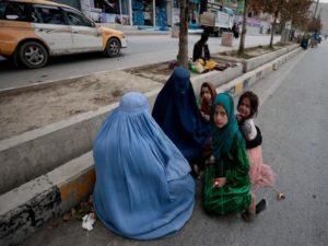 Women wearing burqas sit with their children as the beg along a road in Kabul