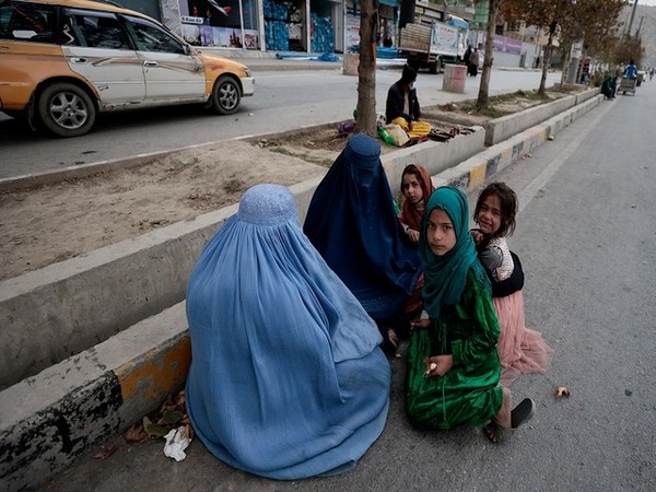 Women wearing burqas sit with their children as the beg along a road in Kabul