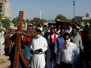 A man holds a cross leading the people carrying coffin of Simon Eric, who was killed in a plane crash, during his burial at the Christian's Gora Cemetery in Karachi