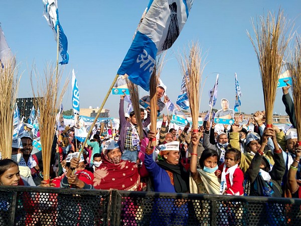 AAP supporters holding party symbol brooms cheer at a public gathering