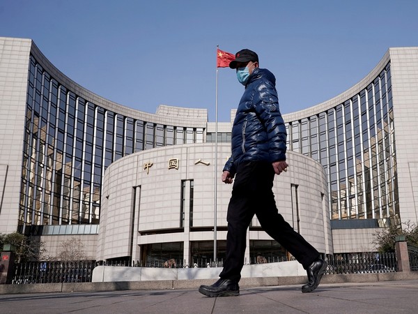 Man wearing a mask walks past the headquarters of the People's Bank of China, the central bank, in Beijing