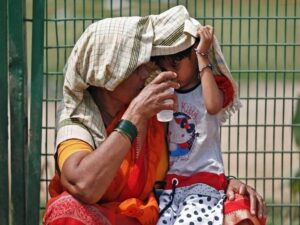 A woman offers water to her granddaughter as she covers her and herself to protect from sun stroke on a hot summer day in New Delhi