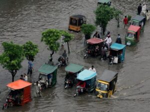 Commuters on rickshaw and motorbikes pass through floodwaters after rain in Lahore